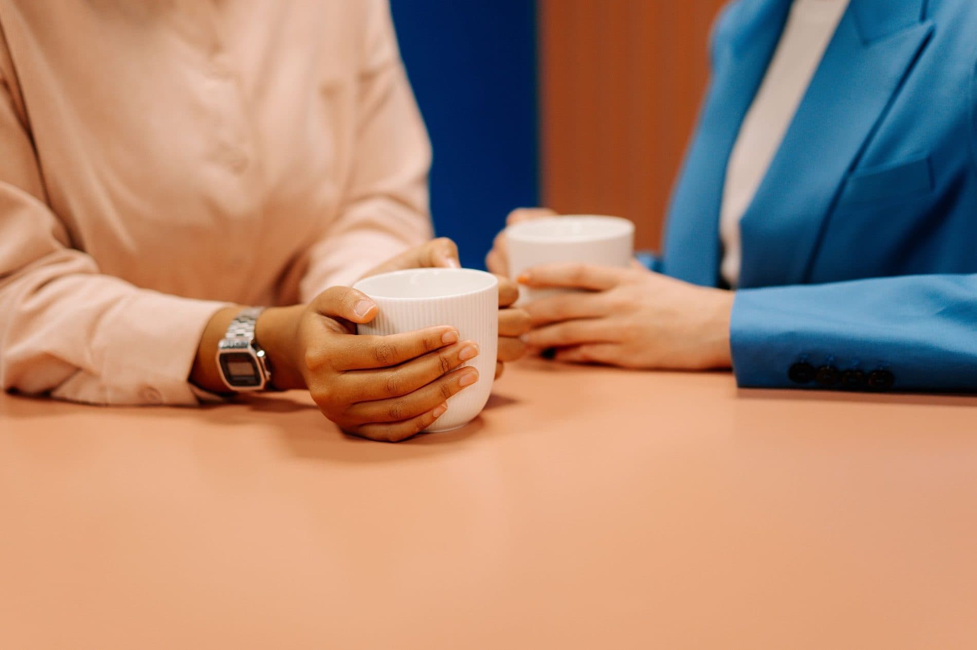 Two people holding coffee cups while talking across a table