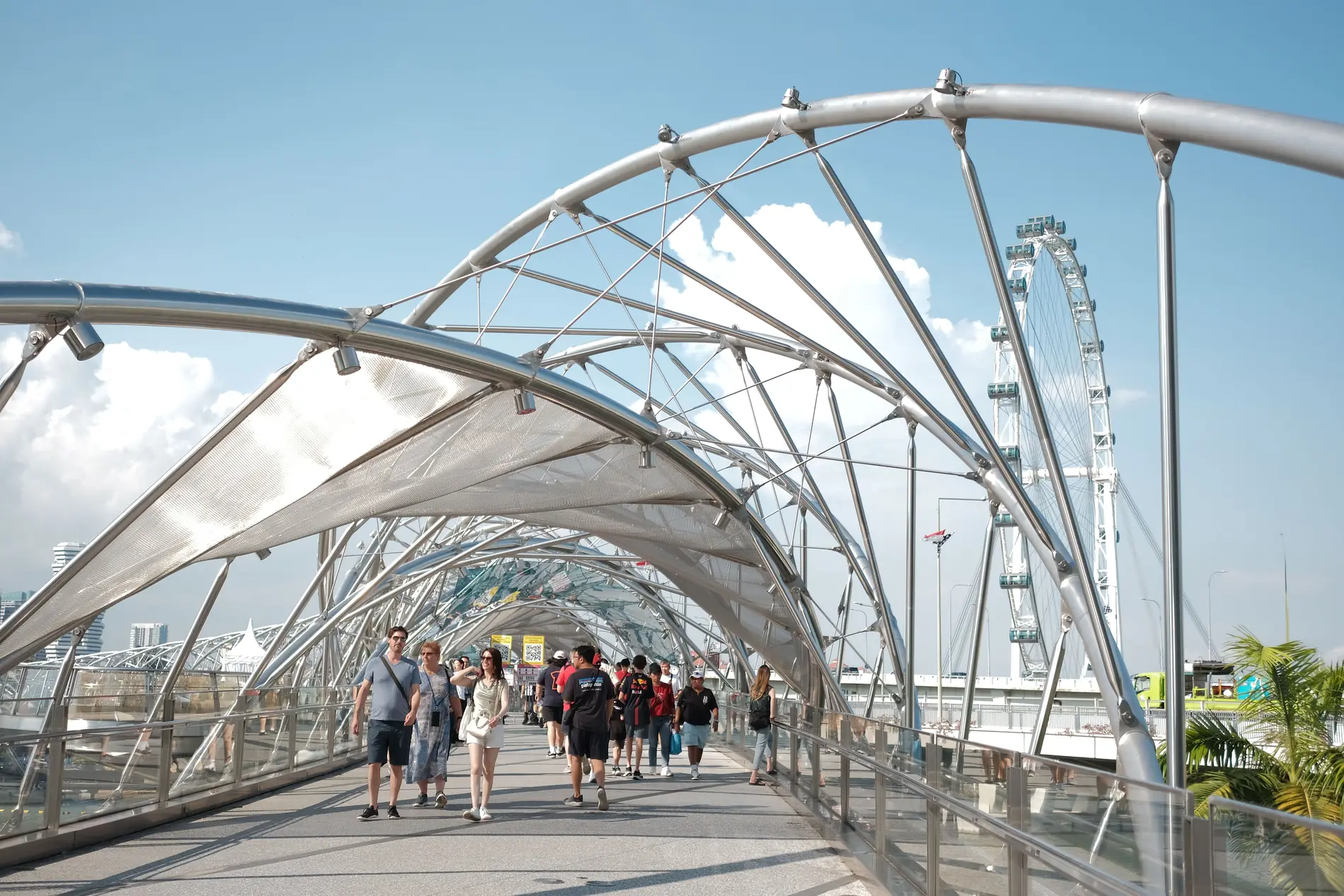 Visitors walking through the Helix Bridge with the Singapore Flyer in the background
